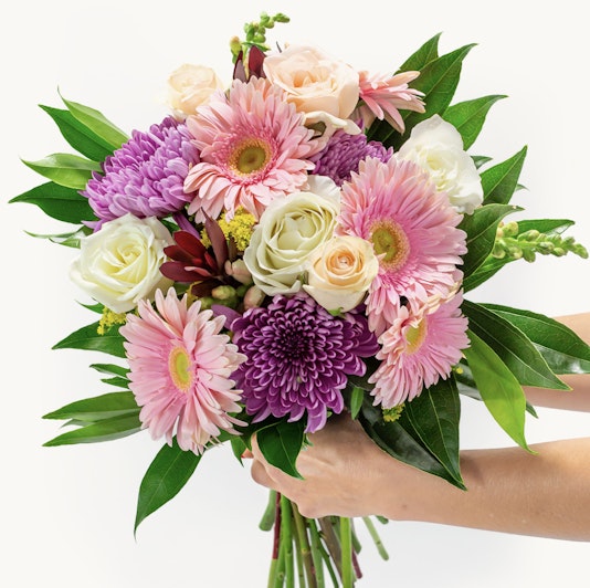 Vibrant spring bouquet featuring pink gerbera daisies, purple flowers, and lush greenery.