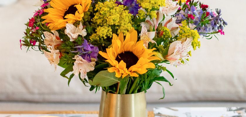 Vibrant floral arrangement featuring sunflowers, colorful blooms, and lush greenery in a gold vase.