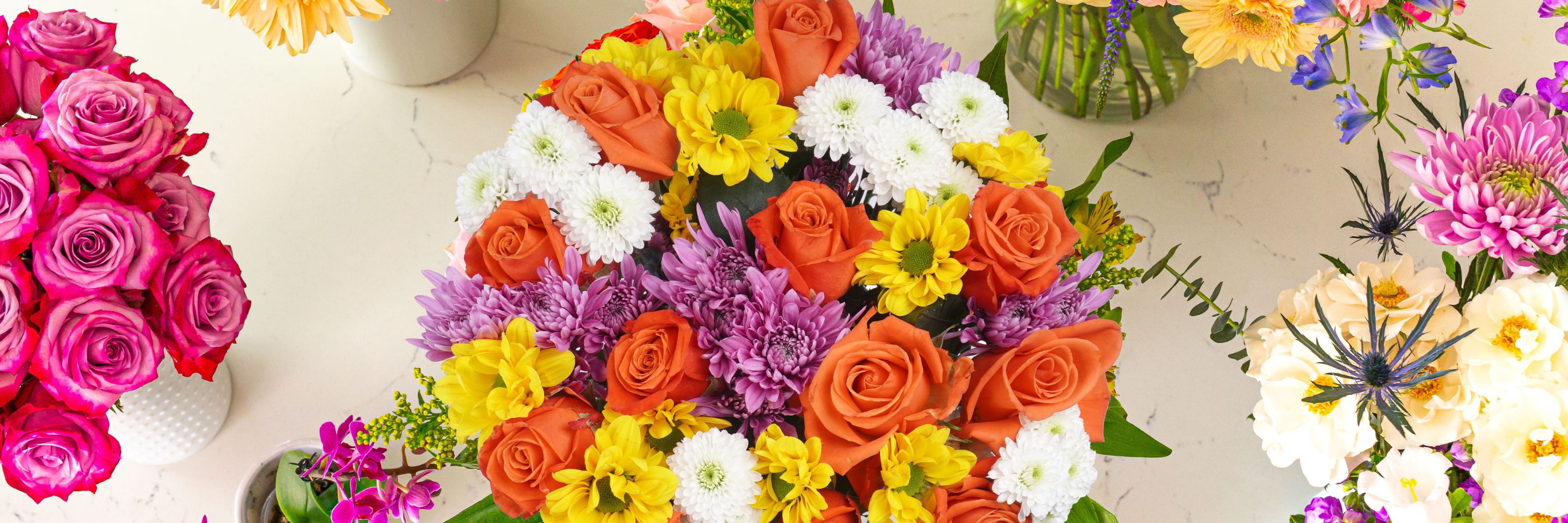 Vibrant floral arrangement featuring orange roses, purple daisies, and cheerful yellow blooms.