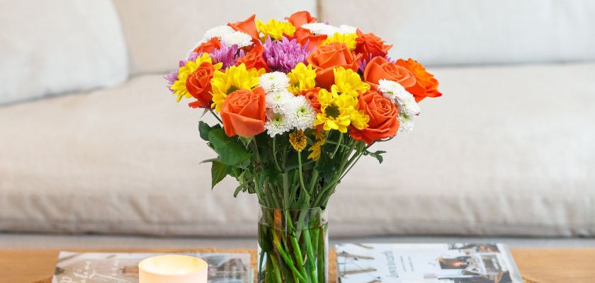 Vibrant mixed flower bouquet featuring orange roses and cheerful daisies in a glass vase.