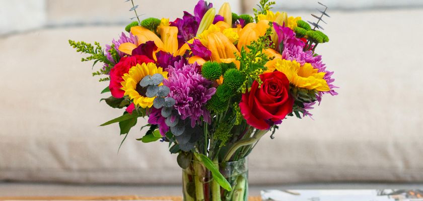 Colorful bouquet featuring sunflowers, roses, and vibrant blooms in a glass vase.