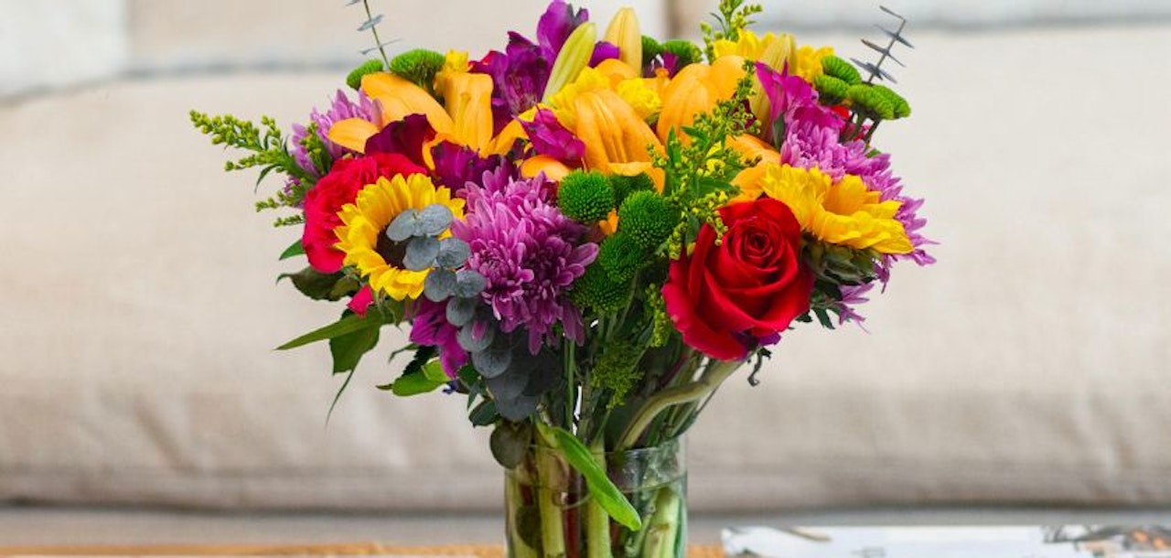 Colorful bouquet featuring sunflowers, roses, and vibrant blooms in a glass vase.