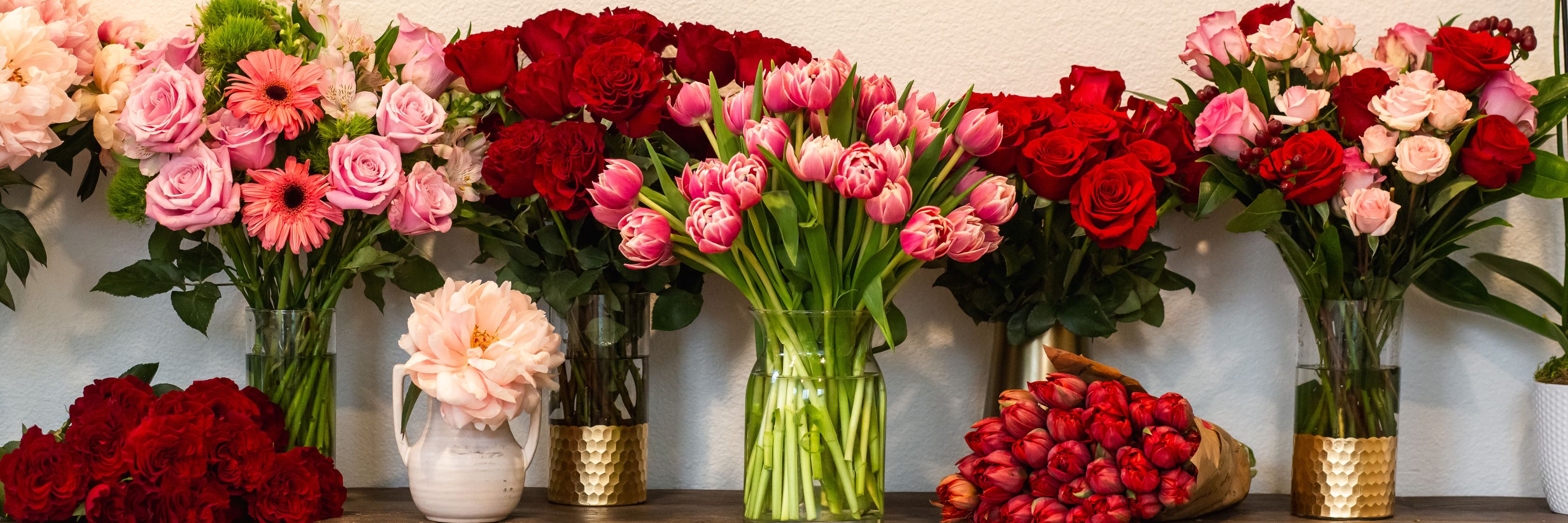 Vibrant floral display featuring red roses, pink tulips, and assorted blooms in elegant vases.