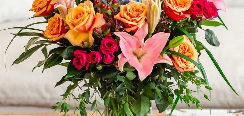 Vibrant floral arrangement featuring orange roses, pink lilies, and lush greenery in a vase.