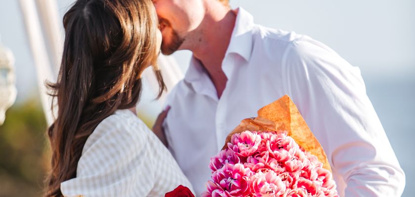 A couple sharing a romantic moment, holding a vibrant bouquet of pink flowers.