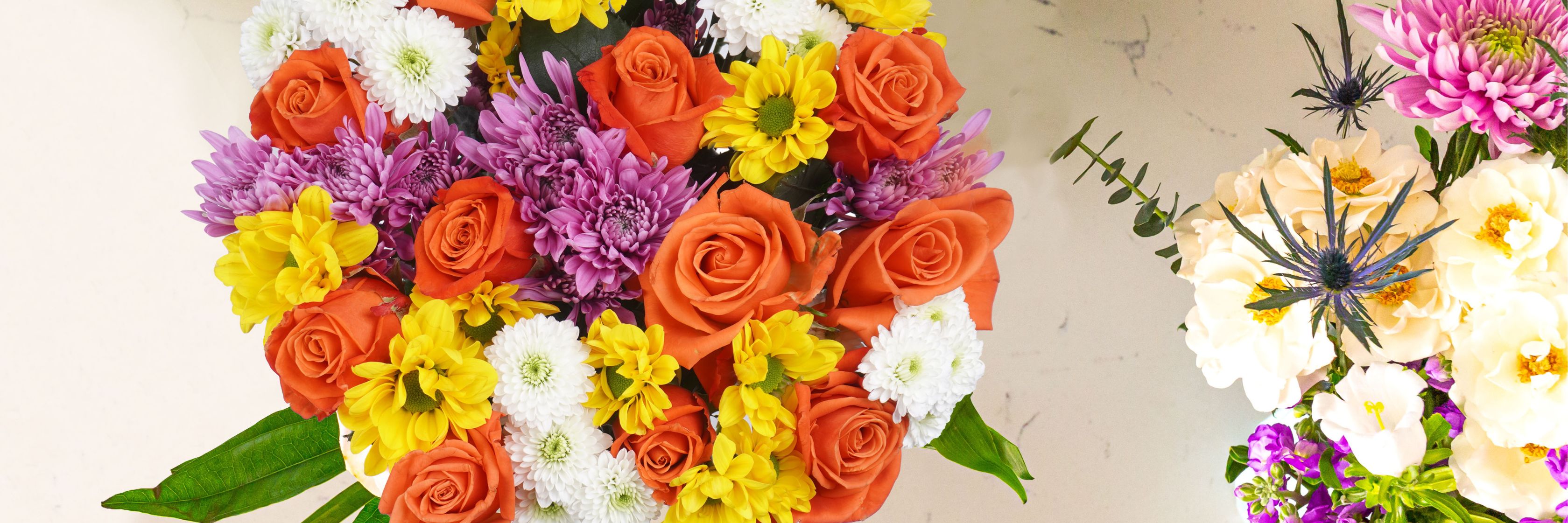 Bright floral arrangement featuring orange roses, purple asters, and cheerful yellow daisies.