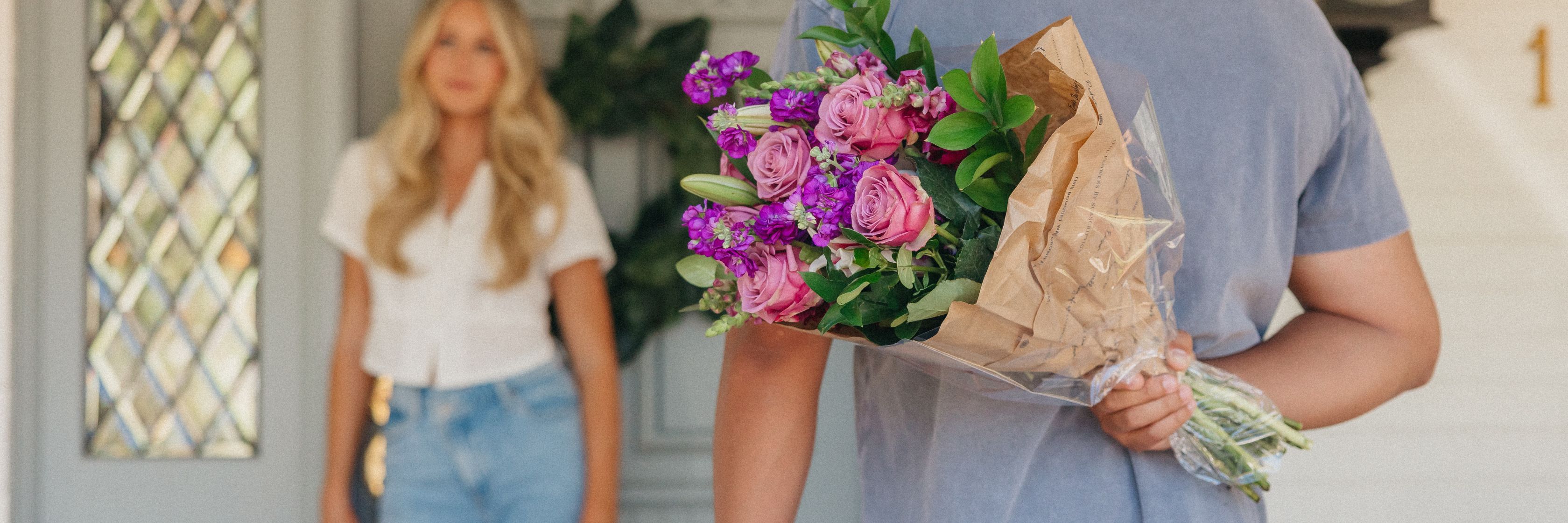 A man delivers a vibrant bouquet of pink and purple flowers to a woman at her door.
