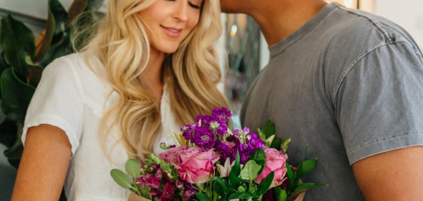 Couple sharing a sweet moment with a vibrant bouquet of mixed pink and purple flowers.