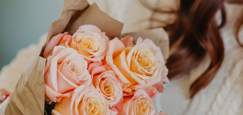 A beautiful bouquet of peach and pink roses wrapped in elegant kraft paper.