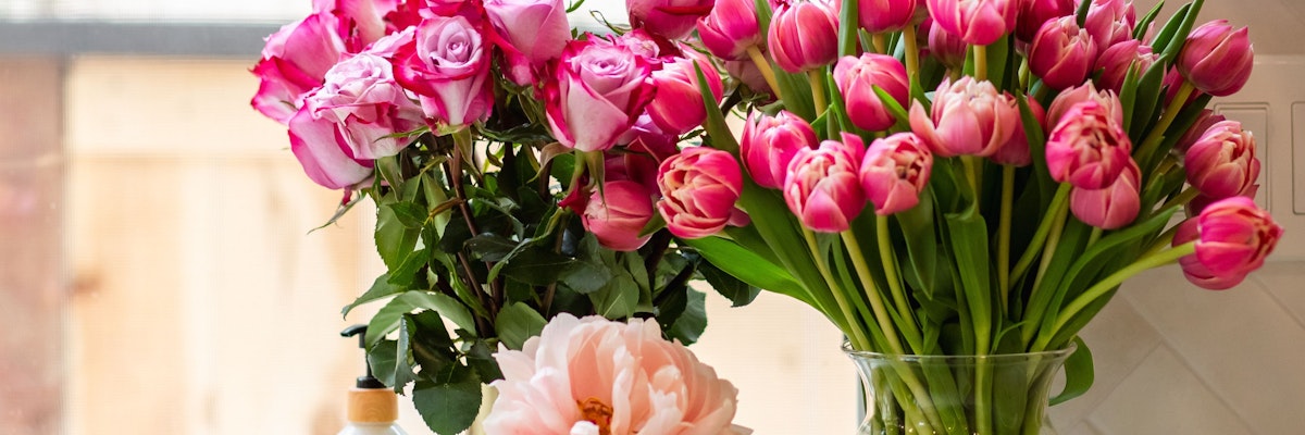 Vibrant mixed bouquet featuring pink roses, tulips, and a peony in a stylish vase.