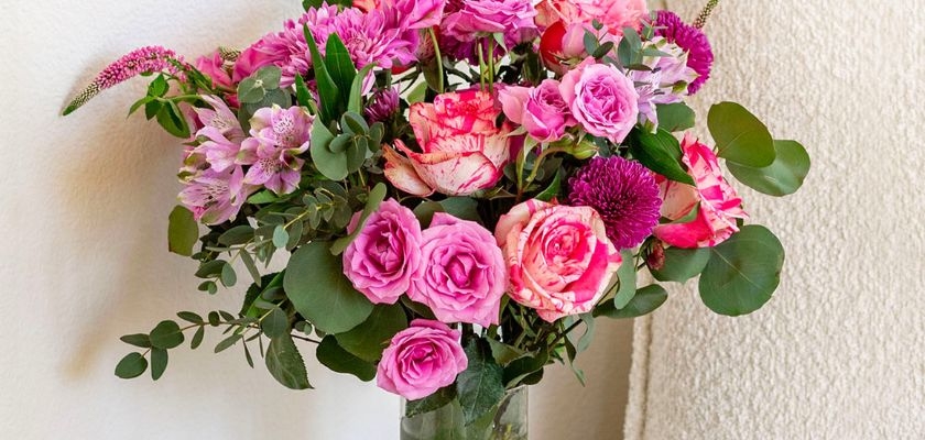 Vibrant pink floral arrangement featuring roses, daisies, and greenery in a glass vase.