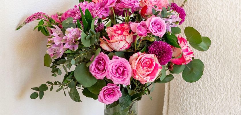 Vibrant pink floral arrangement featuring roses, daisies, and greenery in a glass vase.