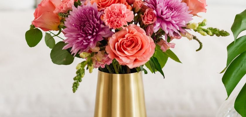 Vibrant floral arrangement featuring pink roses, dahlias, and carnations in a gold vase.