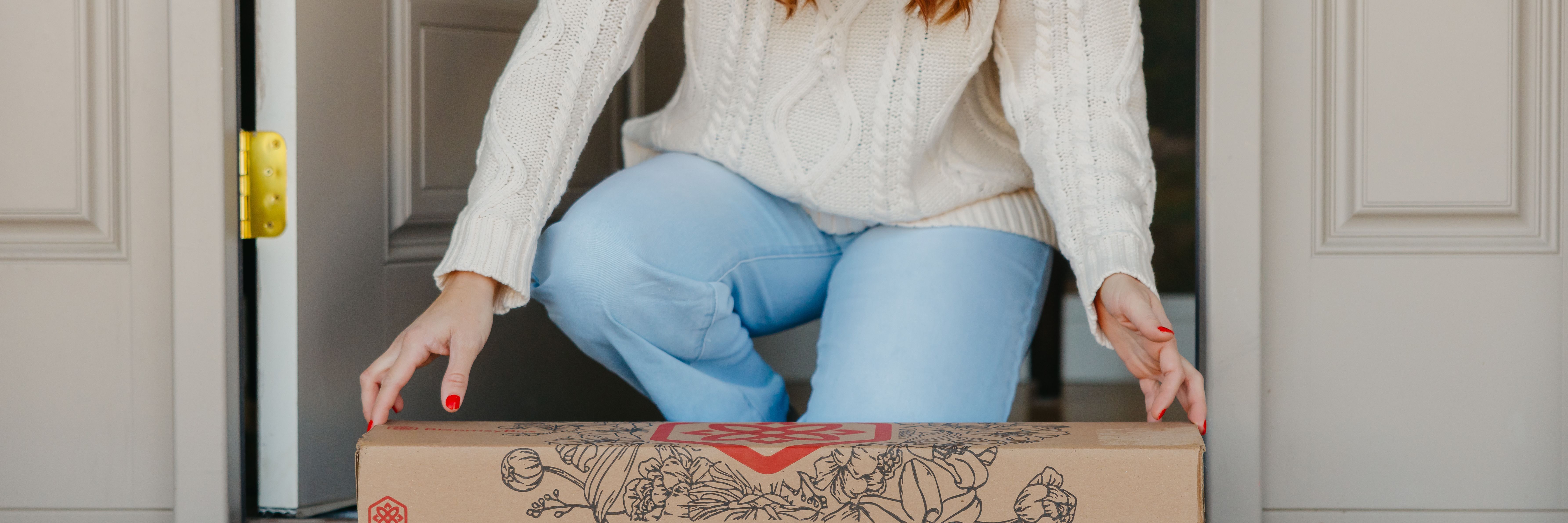 A woman in a cozy sweater receiving a floral delivery box at her doorstep.