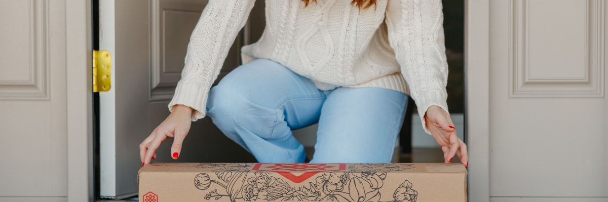 A woman in a cozy sweater receiving a floral delivery box at her doorstep.