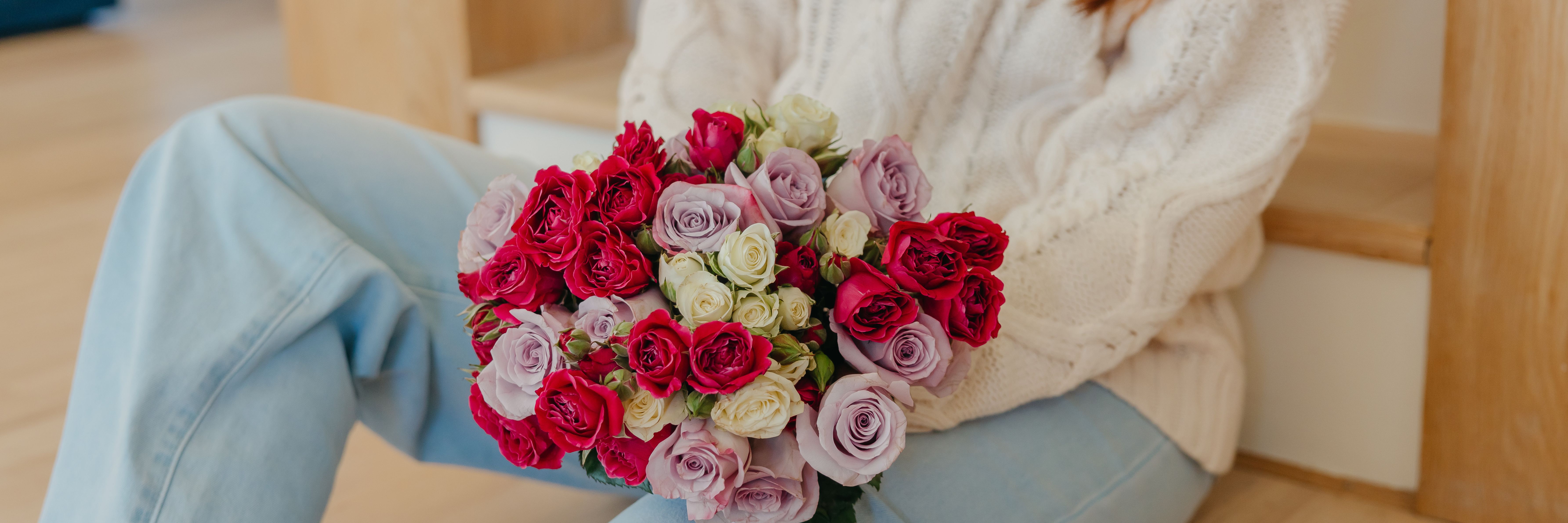 A cozy scene featuring a woman holding a vibrant bouquet of pink and red roses.