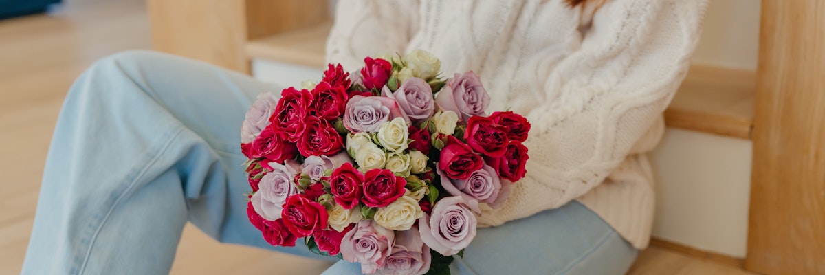 A cozy scene featuring a woman holding a vibrant bouquet of pink and red roses.
