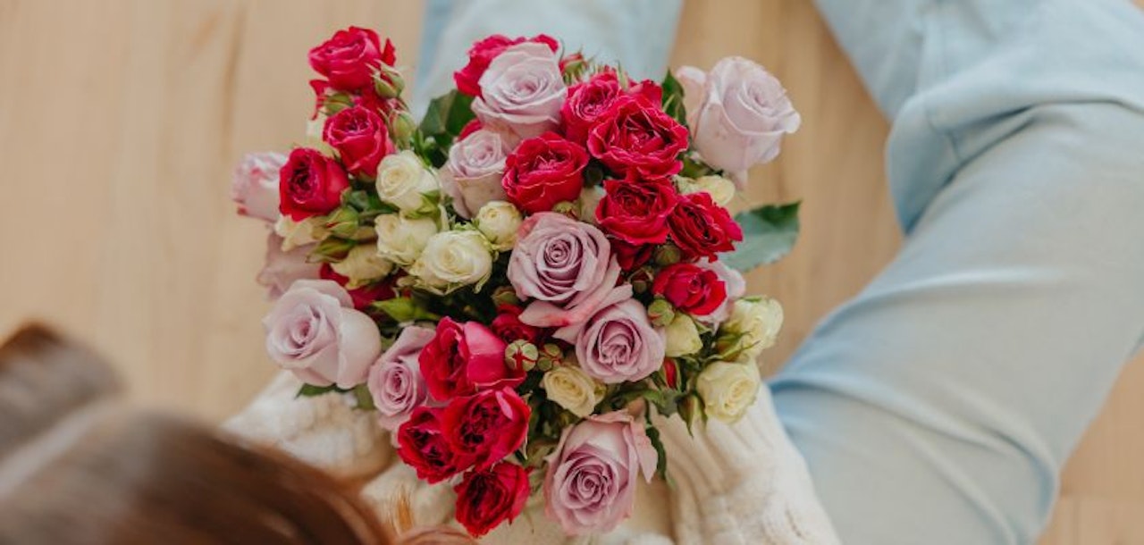 A vibrant bouquet of pink and red roses with white accents, beautifully held in hands.