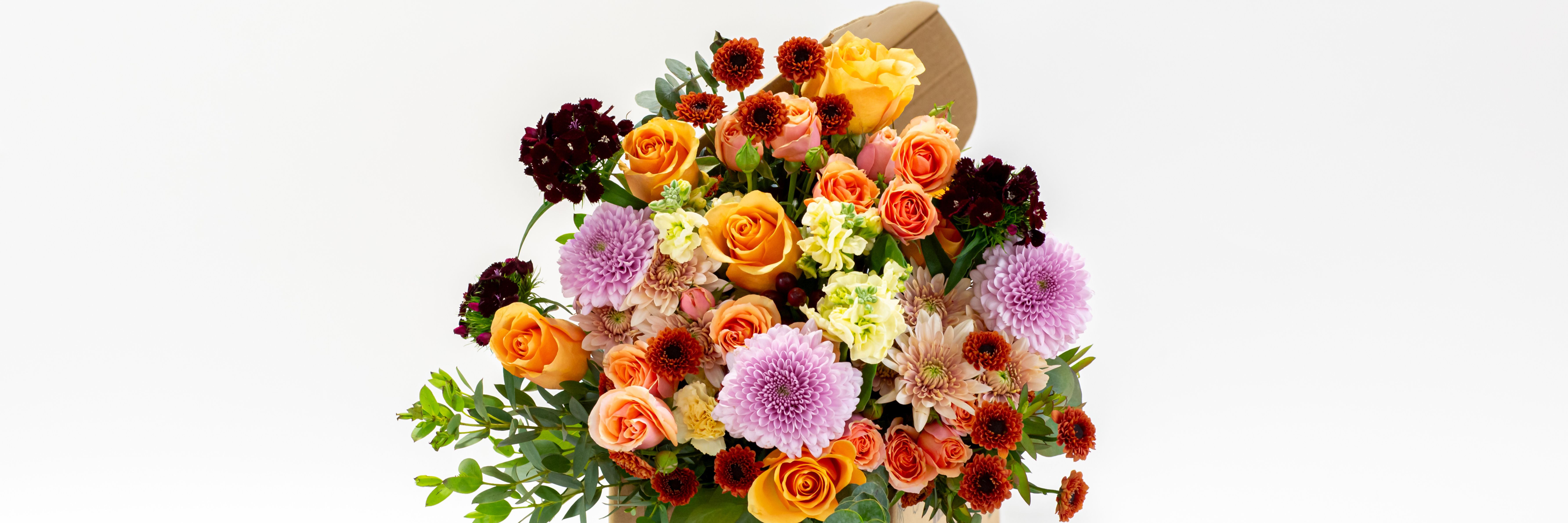 Vibrant bouquet featuring orange roses, purple blooms, and lush greenery, perfect for brightening any occasion.