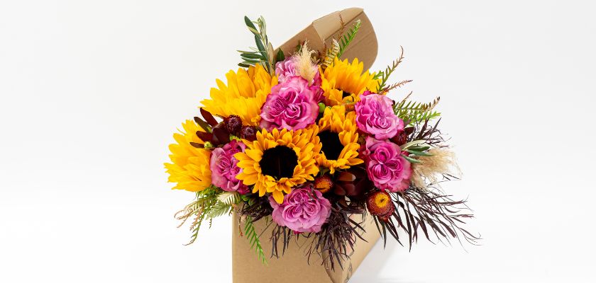 Vibrant arrangement of sunflowers and pink roses in a stylish gift box, perfect for celebrations.