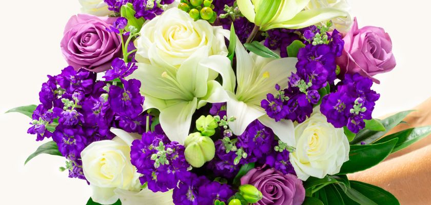 Vibrant bouquet featuring white lilies, purple roses, and colorful blossoms, elegantly arranged.