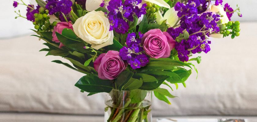 Vibrant floral bouquet featuring purple, pink, and white roses with lush greenery.