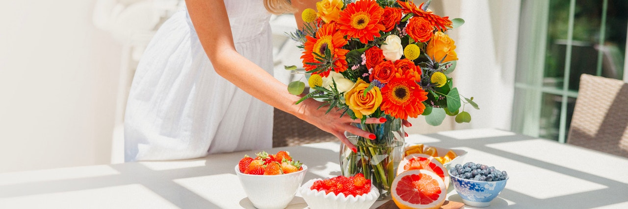 Vibrant bouquet of orange flowers paired with fresh fruit on a sunlit table.