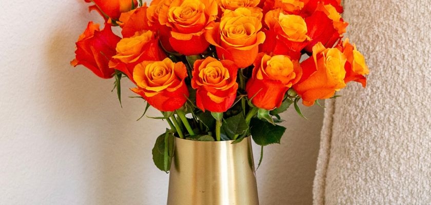 Vibrant orange and yellow roses in a sleek gold vase, perfect for brightening any space.