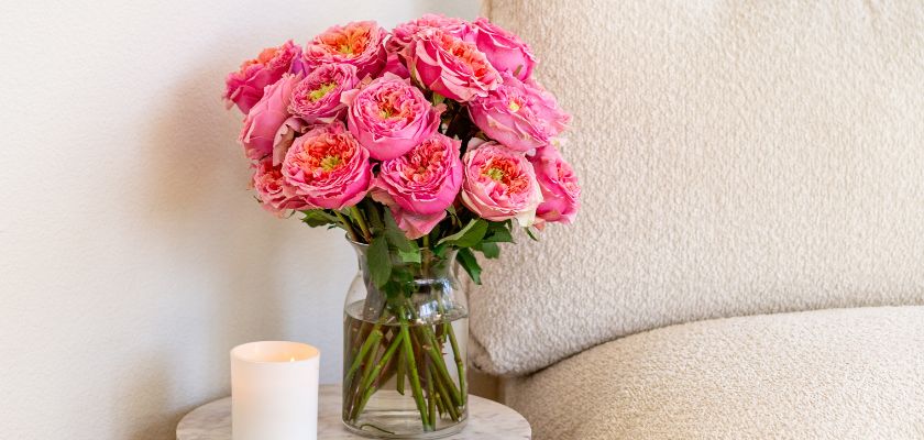 A stunning vase of pink roses beautifully displayed next to a candle on a table.