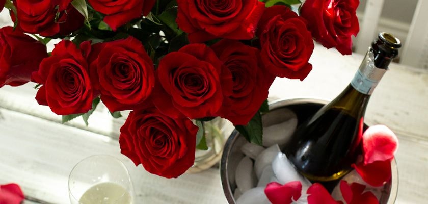 Luxurious red roses paired with chilled champagne, surrounded by delicate rose petals.