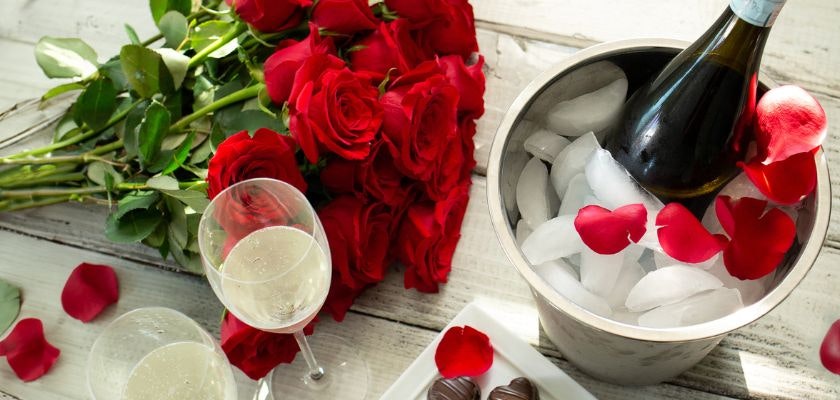 Elegant setting with red roses, champagne, and chocolates for a romantic occasion.