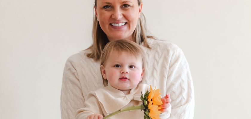 A smiling woman holds a toddler with a flower, showcasing a heartwarming family moment.