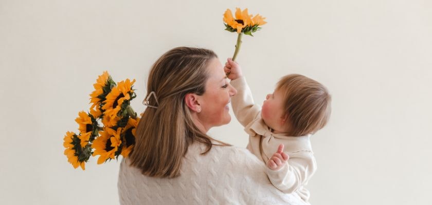 Joyful moment of a mother holding sunflowers while sharing smiles with her baby.