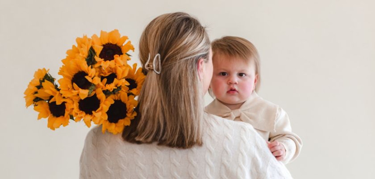 A mother holds her baby close while displaying a cheerful bouquet of sunflowers.