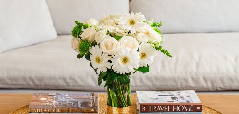 Charming white gerbera daisies and roses in a stylish vase on a coffee table.