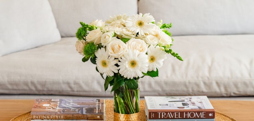 Charming white gerbera daisies and roses in a stylish vase on a coffee table.