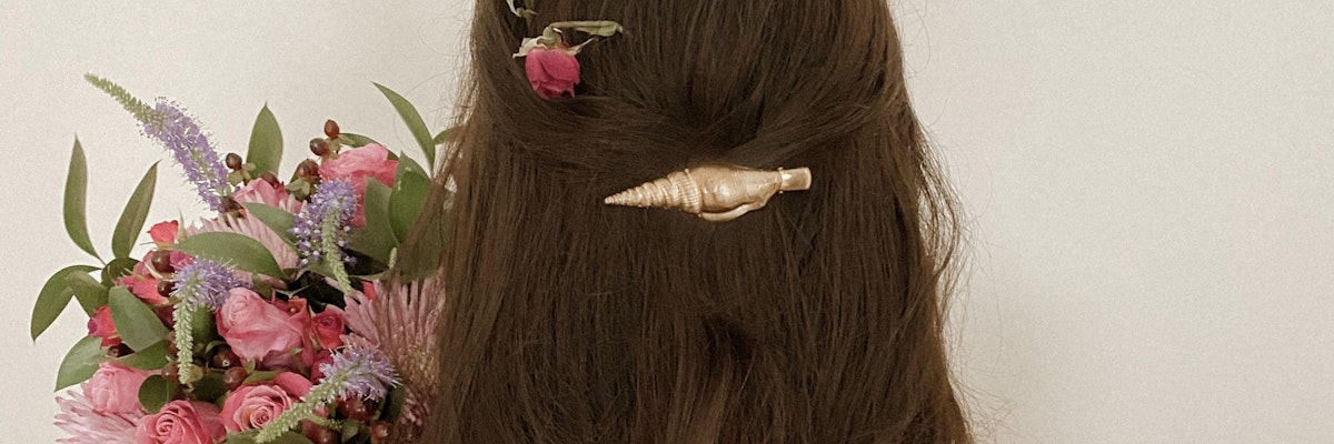 A woman with long brown hair adorned with a floral hairpin and a colorful bouquet.