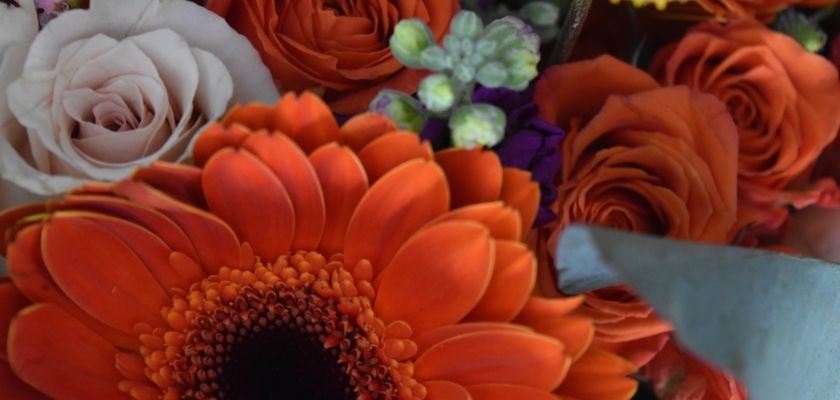 Vibrant floral bouquet featuring orange gerbera daisies, roses, and mixed blooms.