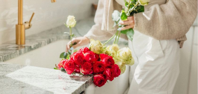 A vibrant bouquet of red and white roses being arranged by a gardener on a sleek countertop.