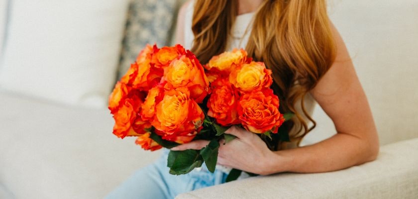 Vibrant bouquet of orange and yellow roses held by a woman, perfect for brightening any space.