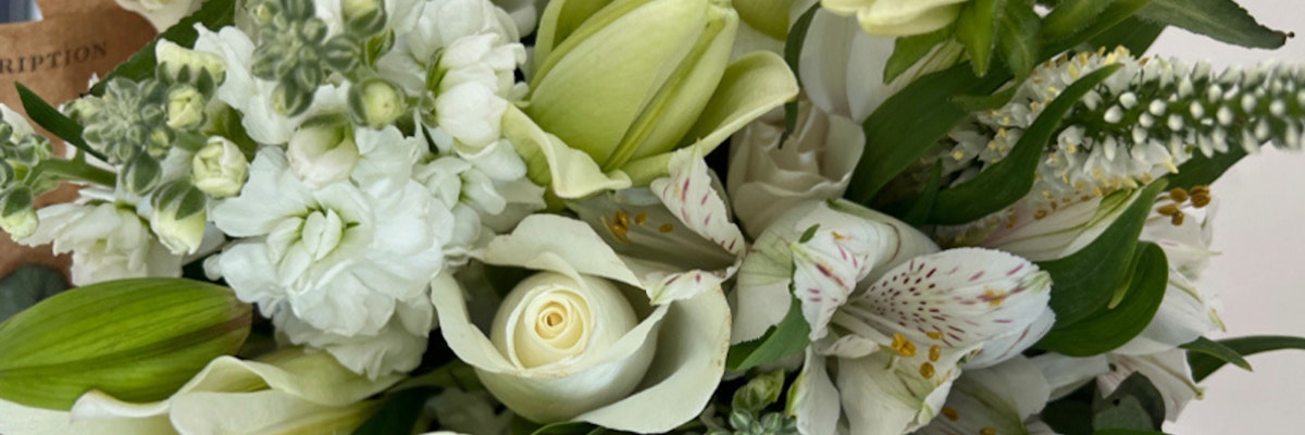 Elegant white floral arrangement featuring roses, lilies, and delicate greenery accents.