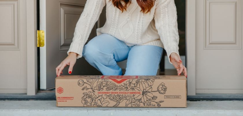 A woman receives a beautifully packaged floral delivery at her doorstep, highlighting gift options.