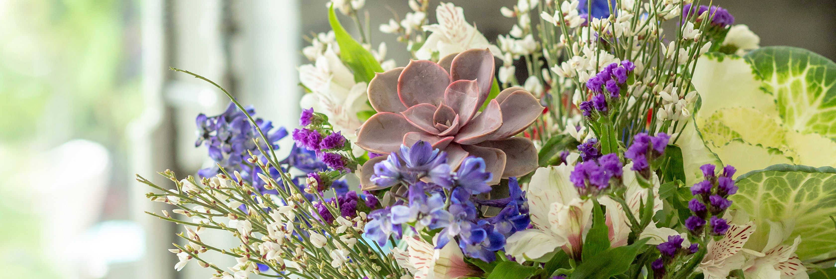 Vibrant floral arrangement featuring purple blooms, succulents, and delicate greenery.