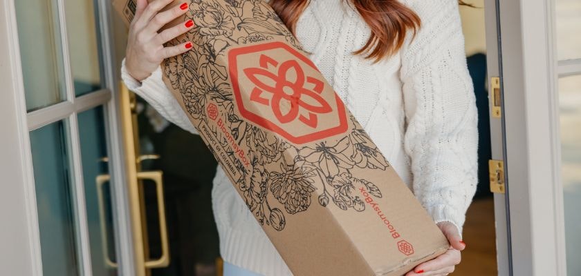 A woman in a cozy sweater joyfully holds a floral delivery box at her door.