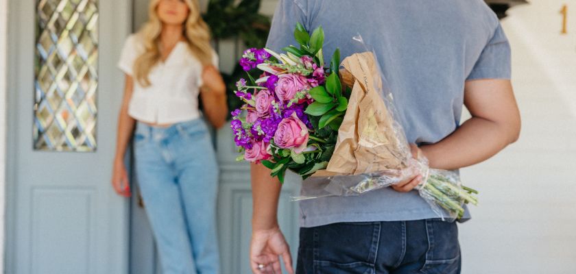 A man surprises a woman at the door with a colorful flower bouquet, creating a romantic moment.