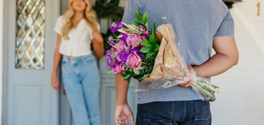 A man surprises a woman at the door with a colorful flower bouquet, creating a romantic moment.