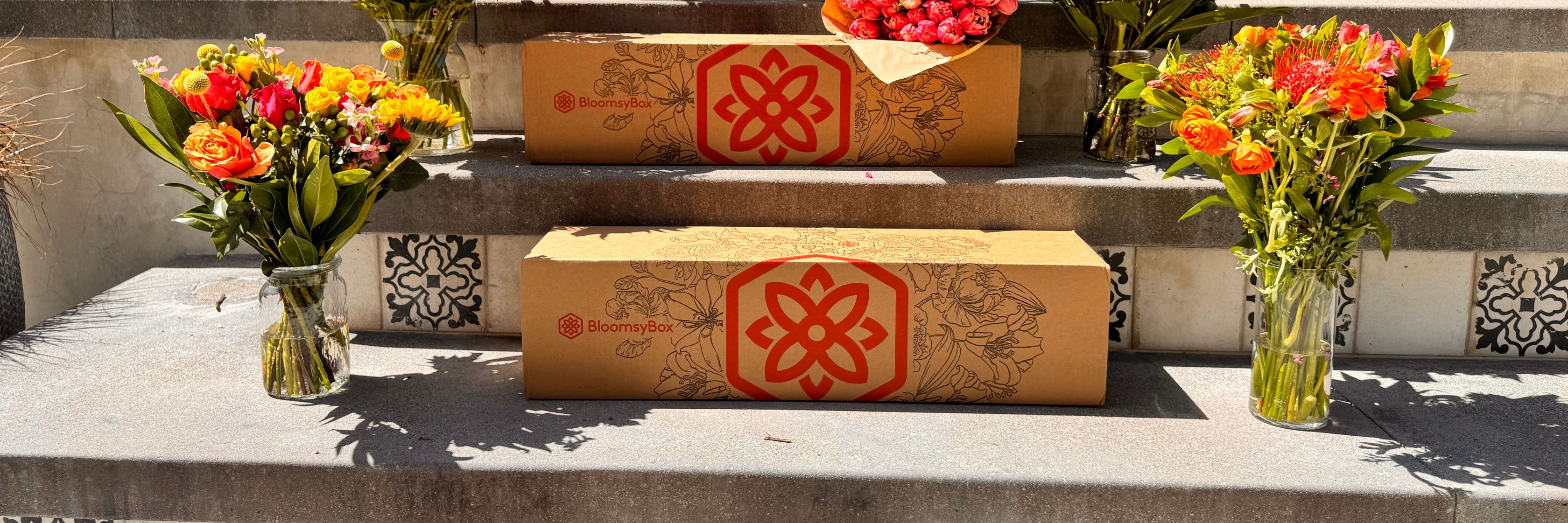 Colorful flower bouquets and BloomsyBox packaging displayed on stone steps.