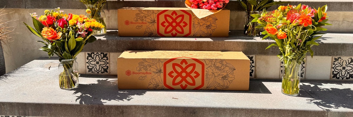 Colorful flower bouquets and BloomsyBox packaging displayed on stone steps.
