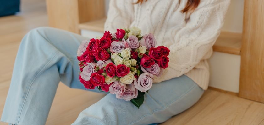 A cozy setting with a woman holding a vibrant bouquet of pink and red roses.