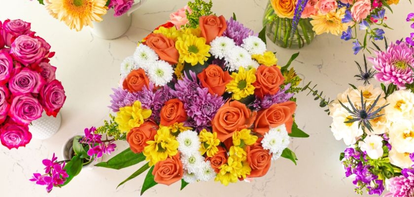 Vibrant floral arrangement with orange roses, daisies, and colorful blooms in elegant vases.